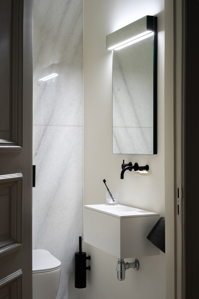 Modern inredning av ett stort vit vitt badrum med dusch, med släta luckor, vita skåp, ett fristående badkar, en vägghängd toalettstol, vit kakel, vita väggar, ett fristående handfat och bänkskiva i akrylsten