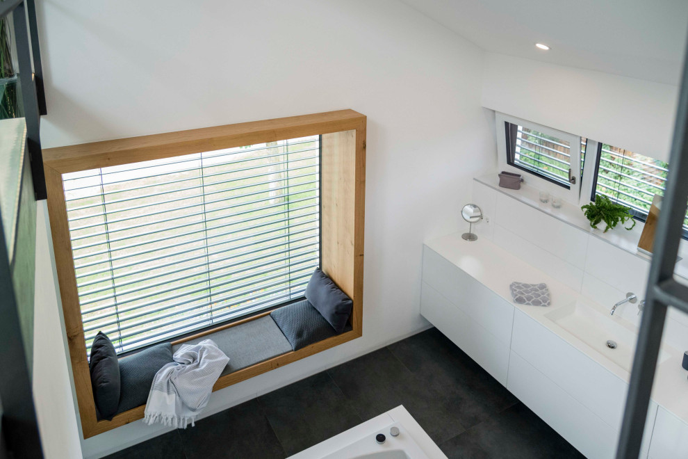 This is an example of a medium sized contemporary bathroom in Munich with white cabinets, white tiles, a built-in sink, solid surface worktops, black floors, white worktops, double sinks and a built in vanity unit.
