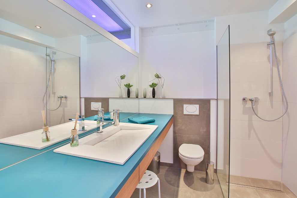 Small industrial shower room bathroom in Cologne with flat-panel cabinets, light wood cabinets, brown tiles, white walls, a built-in sink, beige floors, an open shower, blue worktops, a corner shower and a wall mounted toilet.
