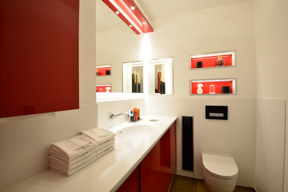 Réalisation d'une salle d'eau design de taille moyenne avec un placard à porte plane, des portes de placard rouges, WC suspendus, un carrelage blanc, des carreaux de porcelaine, un mur blanc, un lavabo intégré et un plan de toilette blanc.