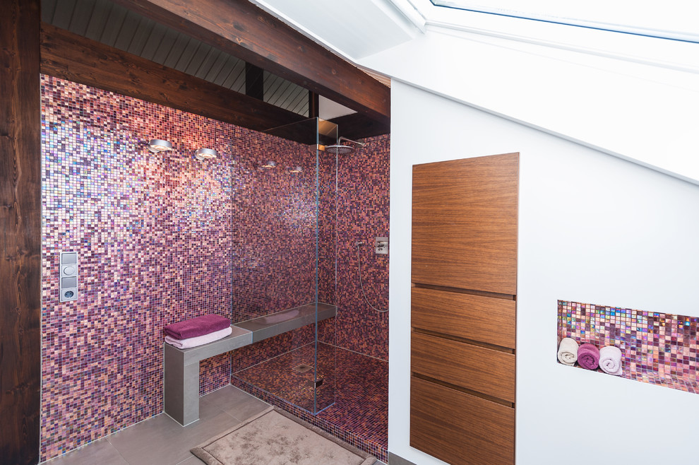 This is an example of a medium sized contemporary shower room bathroom in Frankfurt with a wall-mounted sink, flat-panel cabinets, medium wood cabinets, solid surface worktops, an alcove shower, a wall mounted toilet, pink tiles, mosaic tiles, white walls and ceramic flooring.