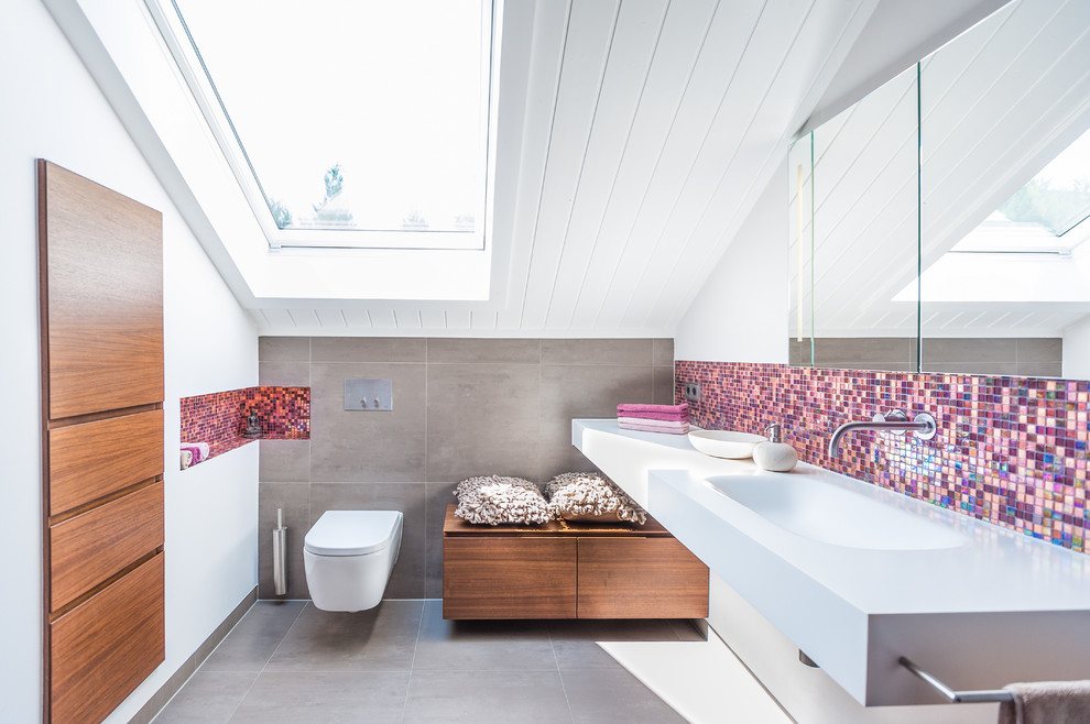 Inredning av ett modernt mellanstort badrum med dusch, med ett väggmonterat handfat, skåp i mellenmörkt trä, bänkskiva i akrylsten, en dusch i en alkov, en vägghängd toalettstol, vita väggar, klinkergolv i keramik, rosa kakel, mosaik och släta luckor