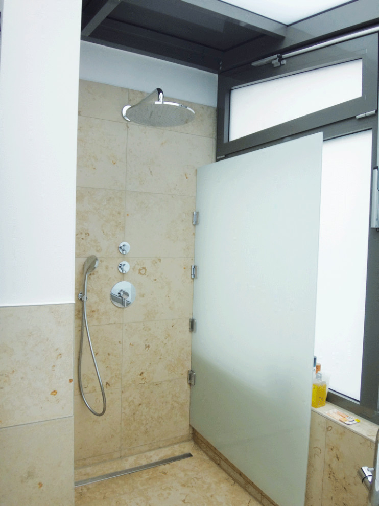 Idéer för mellanstora funkis en-suite badrum, med släta luckor, vita skåp, ett fristående badkar, en kantlös dusch, en vägghängd toalettstol, beige kakel, kakelplattor, vita väggar, kalkstensgolv, ett väggmonterat handfat, beiget golv och med dusch som är öppen