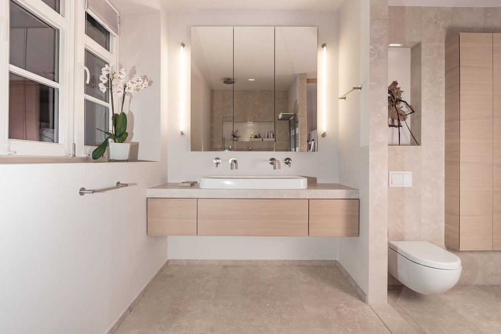 Cette photo montre une salle d'eau tendance en bois brun de taille moyenne avec une douche à l'italienne, WC suspendus, un carrelage beige, du carrelage en pierre calcaire, un mur beige, un sol en calcaire, une vasque, un plan de toilette en calcaire et un sol beige.