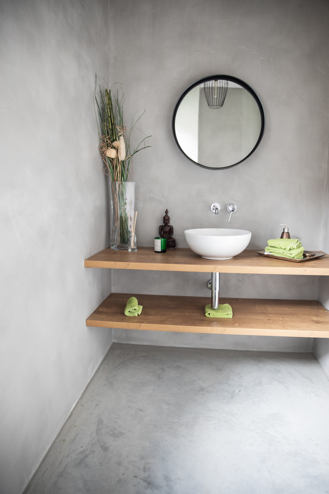 На фото: ванная комната в стиле модернизм с открытыми фасадами, фасадами цвета дерева среднего тона, серыми стенами, бетонным полом, настольной раковиной, столешницей из дерева, серым полом и коричневой столешницей с