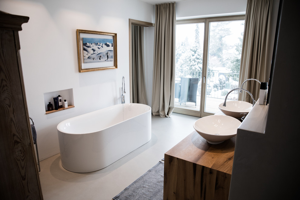 Inspiration för ett mellanstort funkis brun brunt en-suite badrum, med ett fristående badkar, vita väggar, betonggolv, ett fristående handfat, träbänkskiva och grått golv