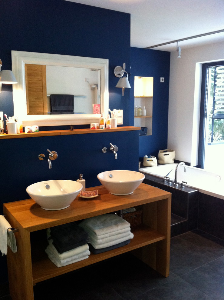 Cette image montre une grande salle d'eau marine en bois brun avec un placard sans porte, une baignoire posée, une douche ouverte, WC séparés, un carrelage gris, des carreaux de céramique, un mur bleu, un sol en carrelage de céramique, une vasque et un plan de toilette en bois.