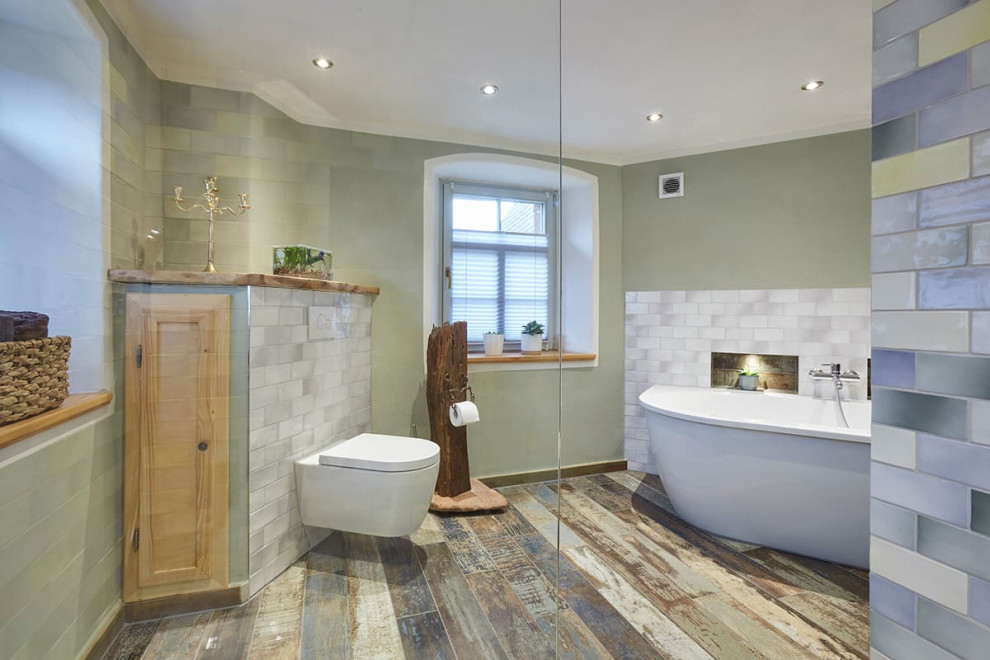 Imagen de cuarto de baño principal rústico grande con bañera exenta, ducha abierta, sanitario de pared, baldosas y/o azulejos grises, paredes verdes, suelo de madera pintada, suelo multicolor y ducha abierta
