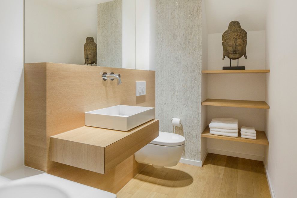 Réalisation d'une salle de bain design en bois brun avec une baignoire posée, WC suspendus, un mur blanc, parquet clair, une vasque, un plan de toilette en bois, un sol marron, un plan de toilette marron et un placard à porte plane.