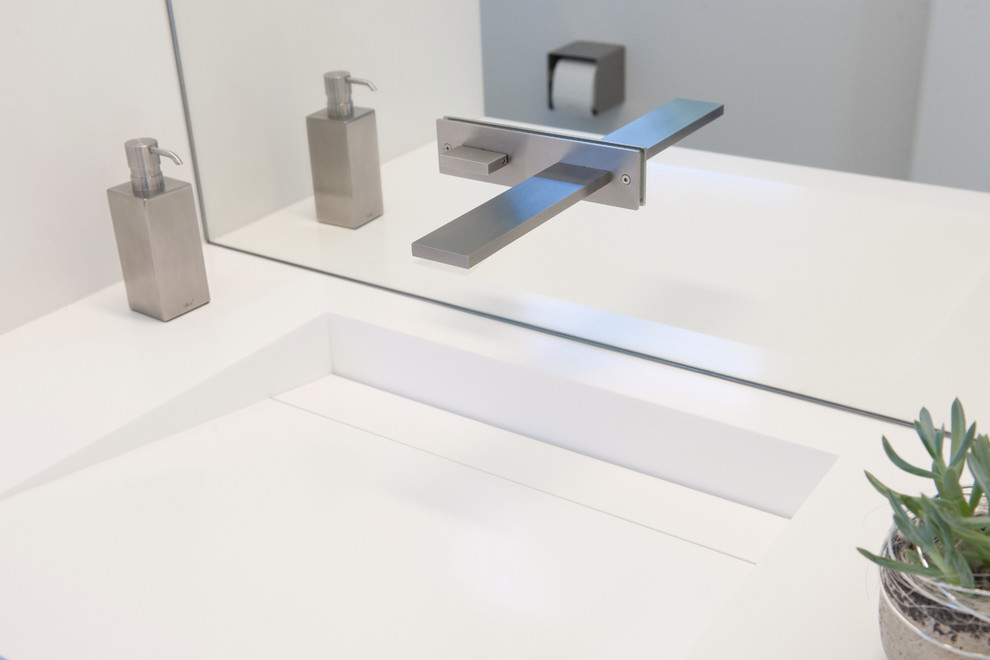 Modelo de cuarto de baño minimalista con puertas de armario blancas, lavabo integrado y encimera de acrílico