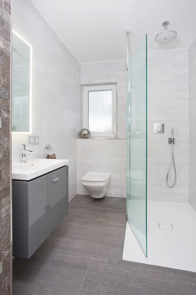 Foto på ett litet funkis badrum med dusch, med släta luckor, grå skåp, en kantlös dusch, en vägghängd toalettstol, grå kakel, keramikplattor, grå väggar, klinkergolv i keramik, ett integrerad handfat, grått golv och med dusch som är öppen