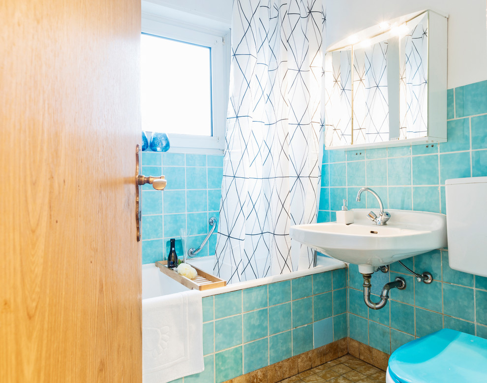 Kleines Mid-Century Duschbad mit Einbaubadewanne, Duschbadewanne, Toilette mit Aufsatzspülkasten, blauen Fliesen, Keramikfliesen, weißer Wandfarbe, Keramikboden, Wandwaschbecken, braunem Boden und Duschvorhang-Duschabtrennung in Sonstige