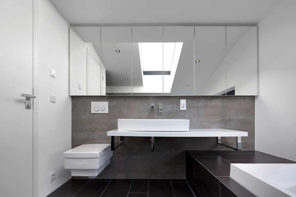Imagen de cuarto de baño actual con bañera encastrada, ducha empotrada, sanitario de pared, baldosas y/o azulejos negros, paredes grises y lavabo sobreencimera