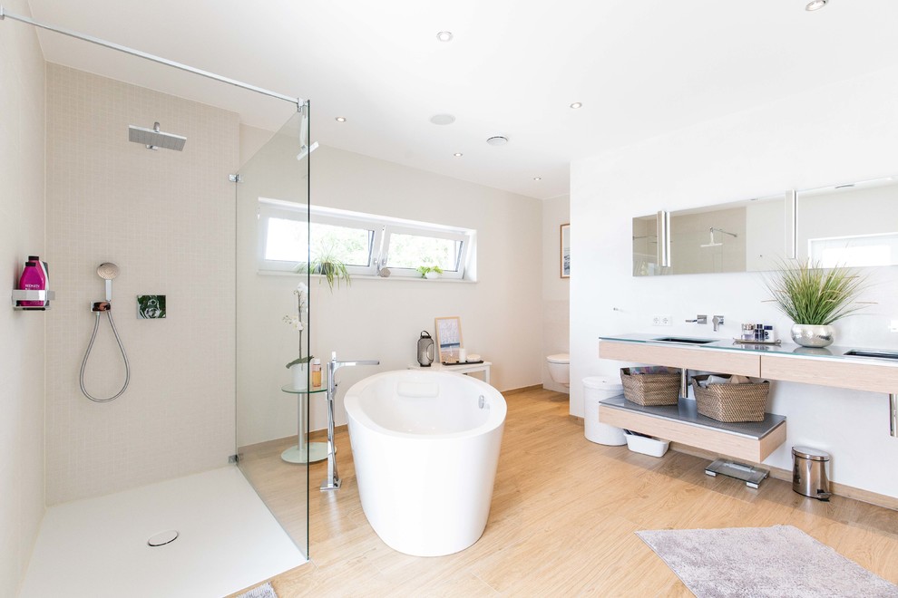 Photo of a large contemporary shower room bathroom in Hanover with open cabinets, beige cabinets, a freestanding bath, a walk-in shower, a wall mounted toilet, white walls, light hardwood flooring, an integrated sink, glass worktops, beige floors, an open shower and blue worktops.