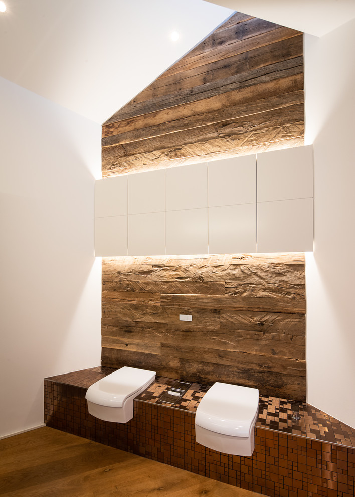 Modelo de cuarto de baño rural de tamaño medio con sanitario de dos piezas, paredes blancas, suelo de madera en tonos medios y suelo marrón