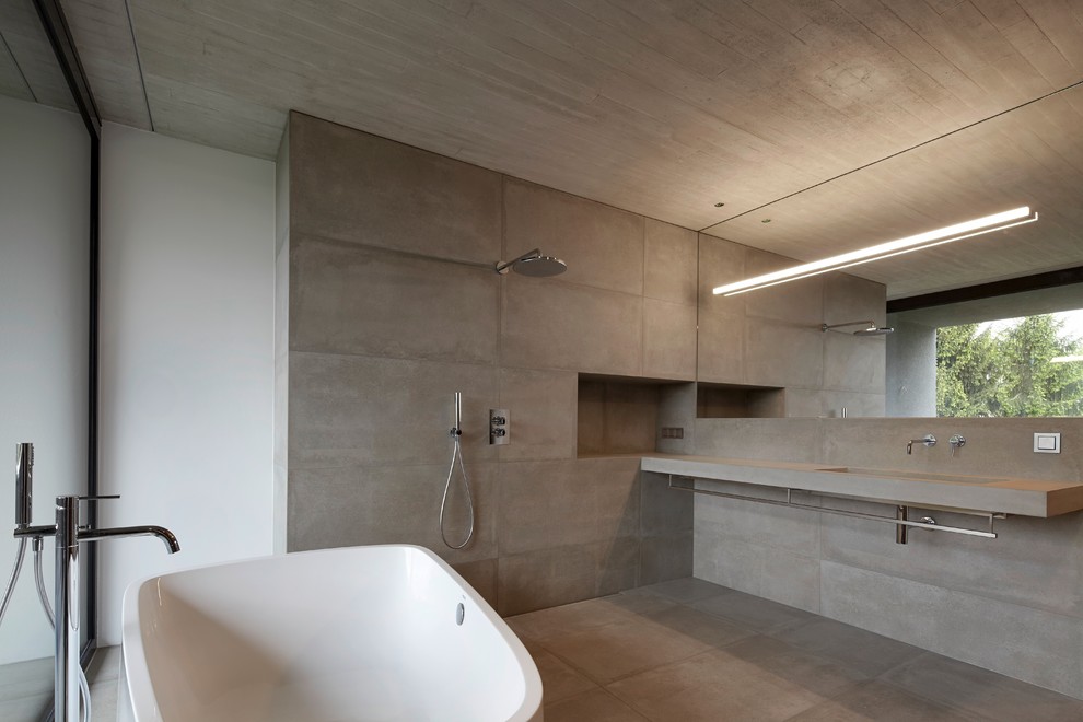 На фото: главная ванная комната среднего размера в современном стиле с монолитной раковиной, отдельно стоящей ванной, открытым душем, серой плиткой, белыми стенами, столешницей из бетона и открытым душем