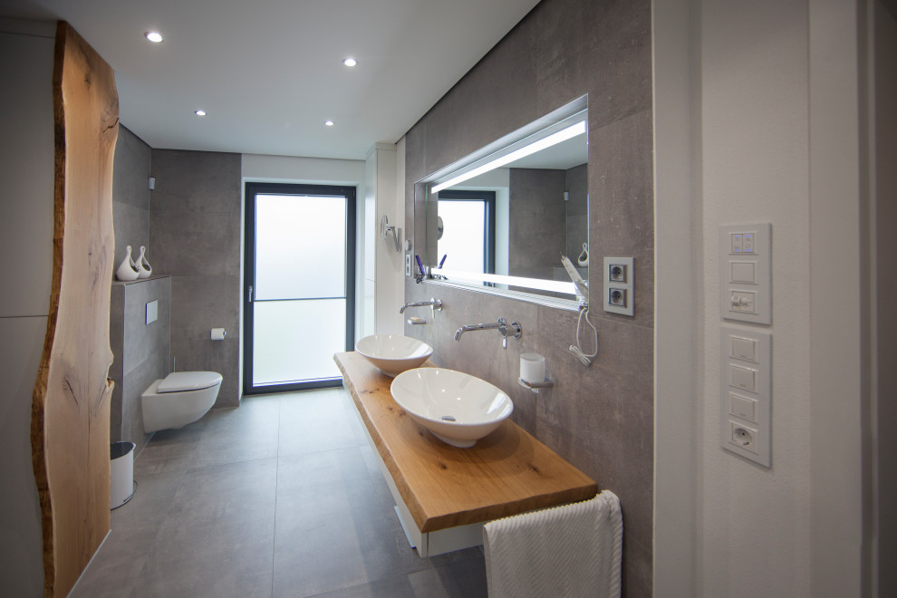 Идея дизайна: большая главная ванная комната в современном стиле с инсталляцией, серой плиткой, белыми стенами, настольной раковиной, столешницей из дерева, серым полом, бежевой столешницей, тумбой под две раковины и подвесной тумбой