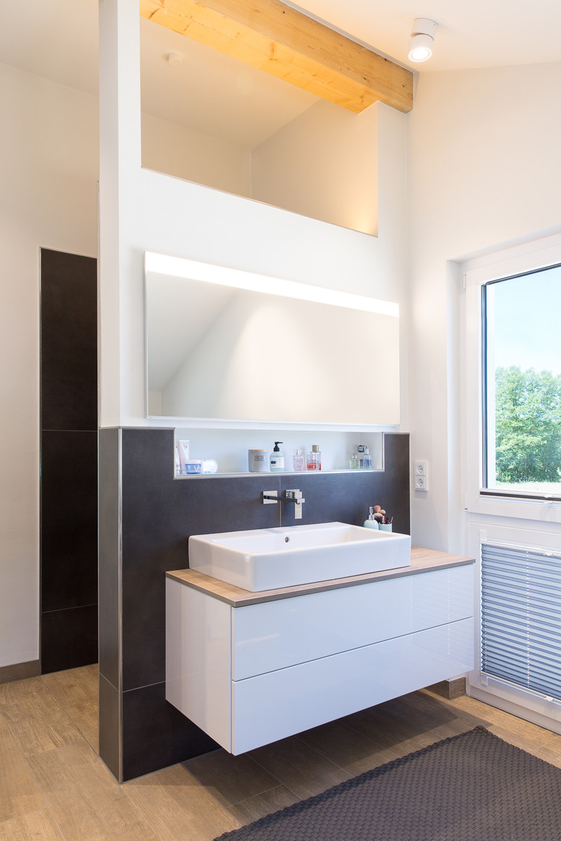 Cette image montre une grande salle de bain design avec des portes de placard blanches, une baignoire en alcôve, une douche ouverte, WC suspendus, un carrelage noir, des carreaux de béton, un mur blanc, carreaux de ciment au sol, une vasque, un sol beige et aucune cabine.