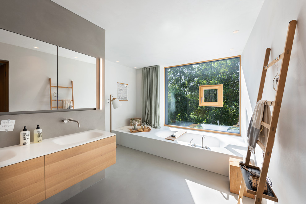 Cette photo montre une très grande salle de bain principale scandinave avec une baignoire en alcôve, des carreaux de miroir, un mur gris, sol en béton ciré, un lavabo intégré, un plan de toilette en bois, un sol gris et un plan de toilette beige.
