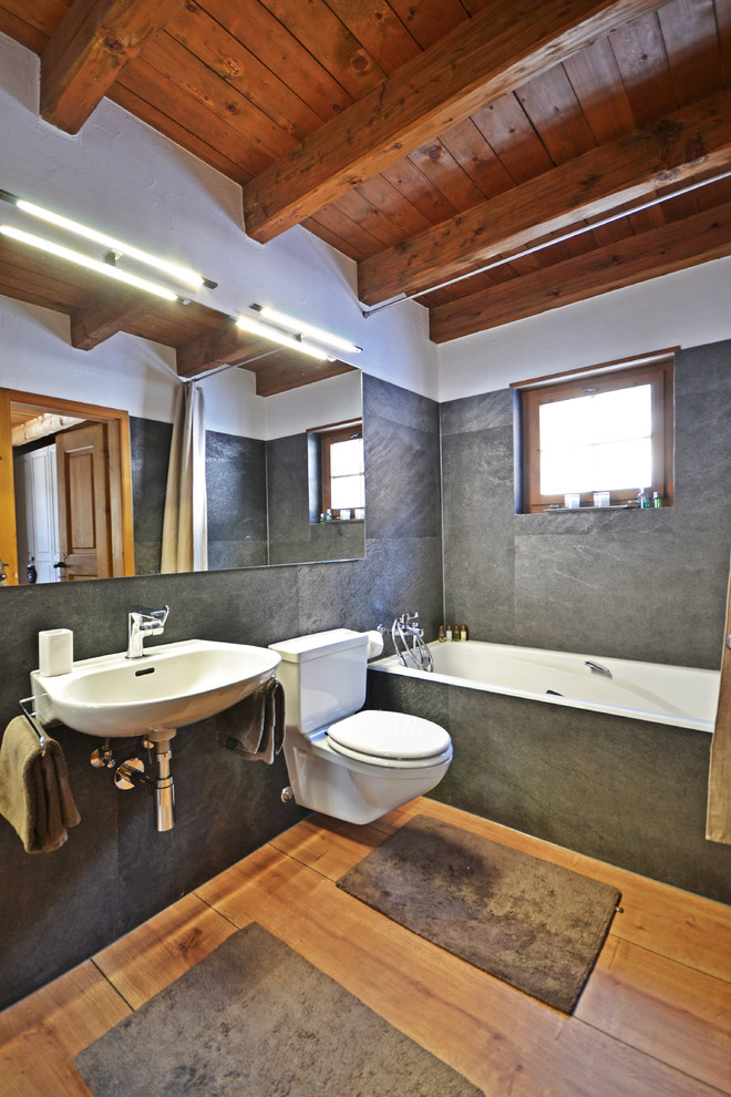 Идея дизайна: серо-белая ванная комната среднего размера в стиле рустика с накладной ванной, раздельным унитазом, серой плиткой, белыми стенами, паркетным полом среднего тона, подвесной раковиной и коричневым полом