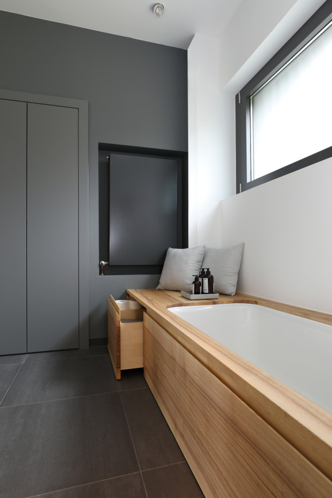 Photo of a medium sized modern ensuite bathroom in Frankfurt with flat-panel cabinets, light wood cabinets, a submerged bath, a built-in shower, a one-piece toilet, grey tiles, white walls, a vessel sink, solid surface worktops, grey floors, a shower curtain, a wall niche, double sinks and a floating vanity unit.