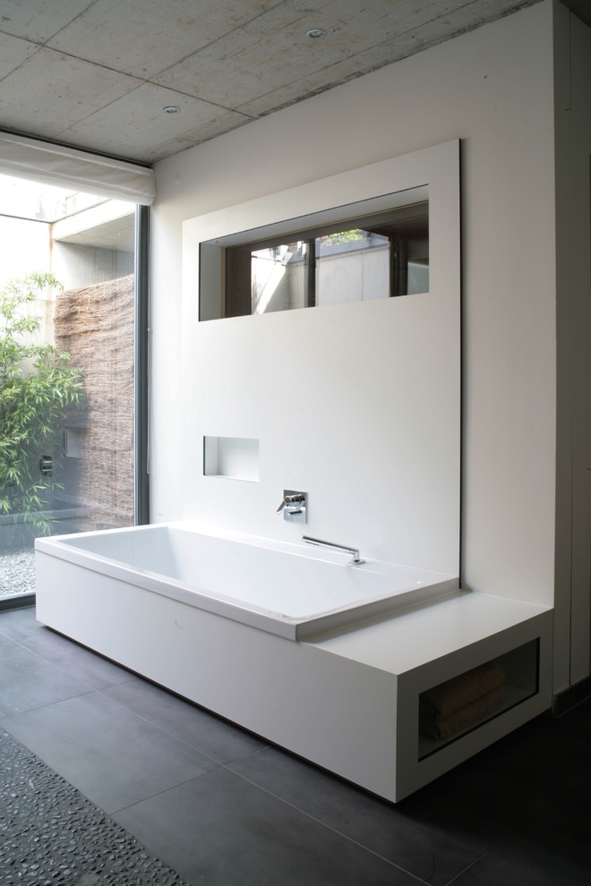 Cette image montre une grande salle de bain design avec une baignoire posée, un mur blanc et un sol en galet.