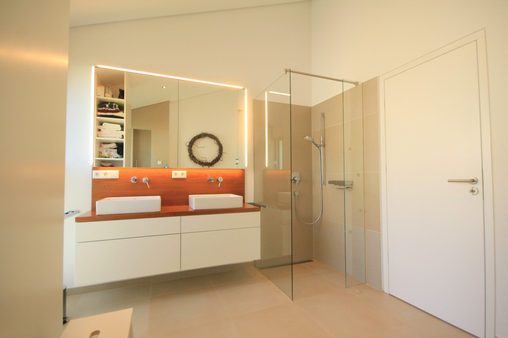 Example of a mid-sized trendy beige tile and stone slab ceramic tile and beige floor bathroom design in Munich with a wall-mount toilet, beige walls, a vessel sink, wood countertops and brown countertops