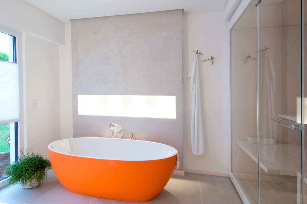 Design ideas for a large contemporary bathroom in Cologne with white cabinets, a freestanding bath, a wall mounted toilet, grey tiles, ceramic tiles, grey walls and solid surface worktops.