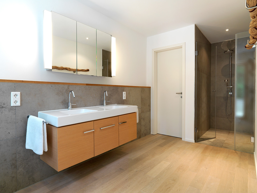 Großes Modernes Badezimmer mit integriertem Waschbecken, flächenbündigen Schrankfronten, hellbraunen Holzschränken, grauen Fliesen, weißer Wandfarbe, braunem Holzboden und Duschnische in Nürnberg