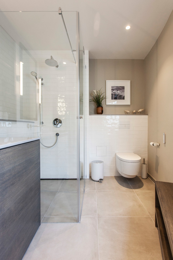 Exemple d'une salle de bain bord de mer de taille moyenne avec un placard à porte plane, une douche à l'italienne, WC suspendus, un carrelage métro, un mur beige, un plan de toilette en bois, un sol beige et une cabine de douche à porte battante.