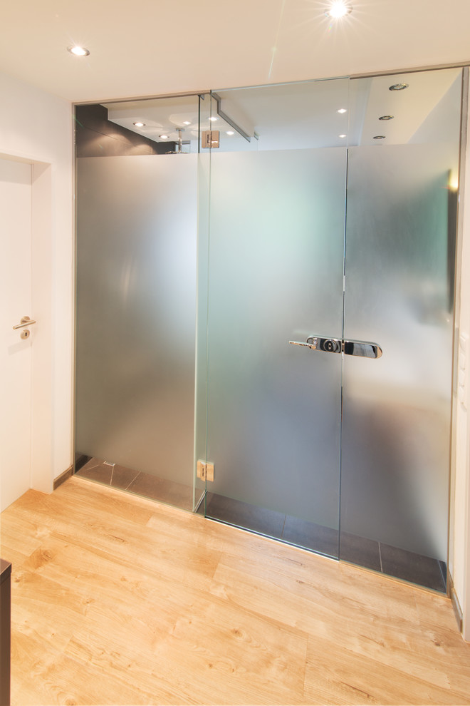 Kleines Modernes Duschbad mit Wandwaschbecken, bodengleicher Dusche, Wandtoilette, grauen Fliesen, Keramikfliesen, weißer Wandfarbe und Vinylboden in Sonstige