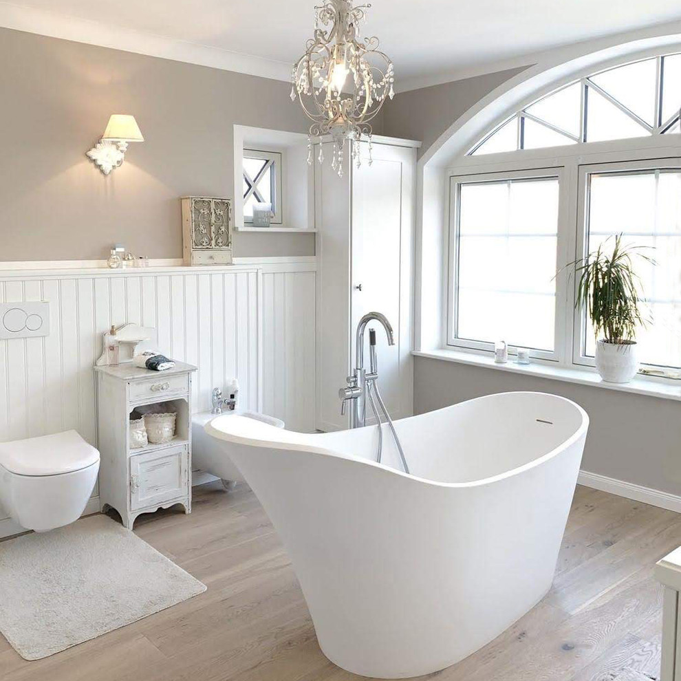 Diseño de cuarto de baño romántico con bañera exenta, sanitario de pared, paredes beige, suelo de madera clara y suelo marrón