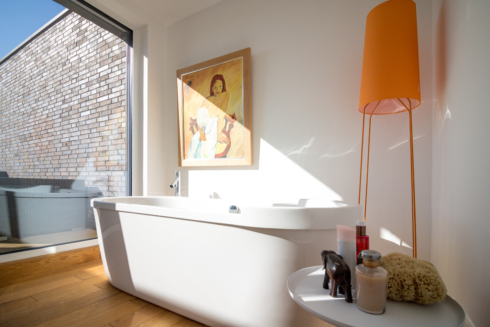 Ejemplo de cuarto de baño minimalista con bañera exenta, paredes blancas, suelo de madera clara y suelo naranja