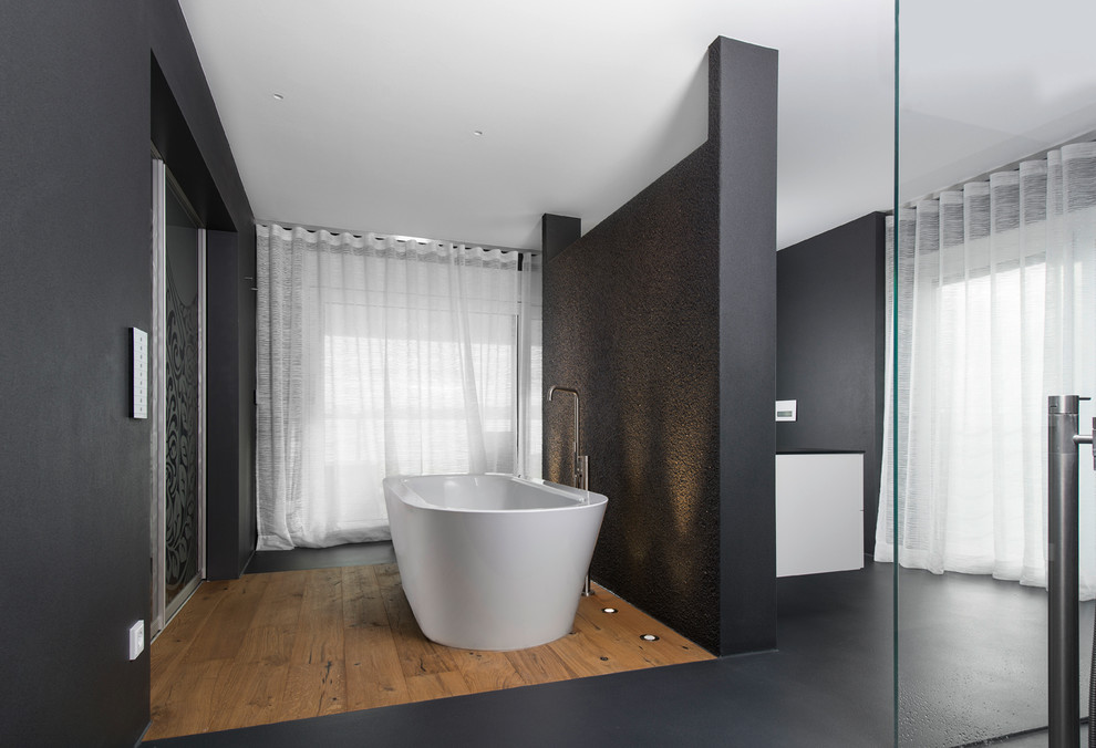 Exemple d'une grande salle de bain principale tendance avec une baignoire indépendante, un mur noir et un sol en bois brun.