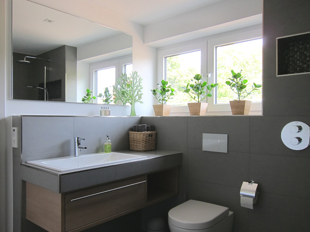 Contemporary shower room bathroom in Cologne with light wood cabinets, tiled worktops, grey tiles, ceramic tiles, white walls, ceramic flooring, a built-in sink, a built-in shower and a wall mounted toilet.