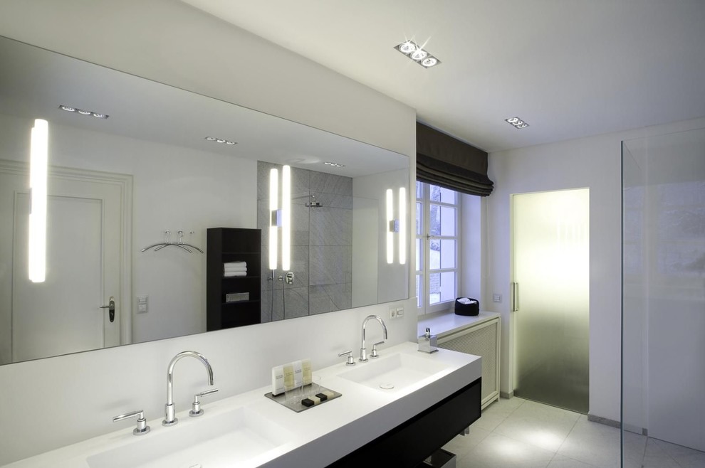 Idées déco pour une très grande salle de bain contemporaine avec un placard à porte plane, des portes de placard noires, un carrelage gris, un carrelage de pierre, un mur blanc, un lavabo intégré et un plan de toilette en surface solide.
