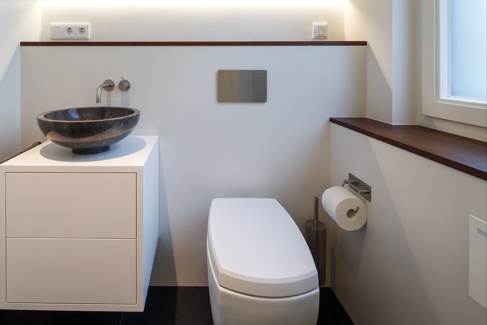 Réalisation d'un WC et toilettes design de taille moyenne avec un placard à porte plane, des portes de placard blanches, WC séparés, un carrelage blanc, du carrelage en marbre, un mur blanc, un sol en calcaire, une vasque, un plan de toilette en bois et un sol gris.