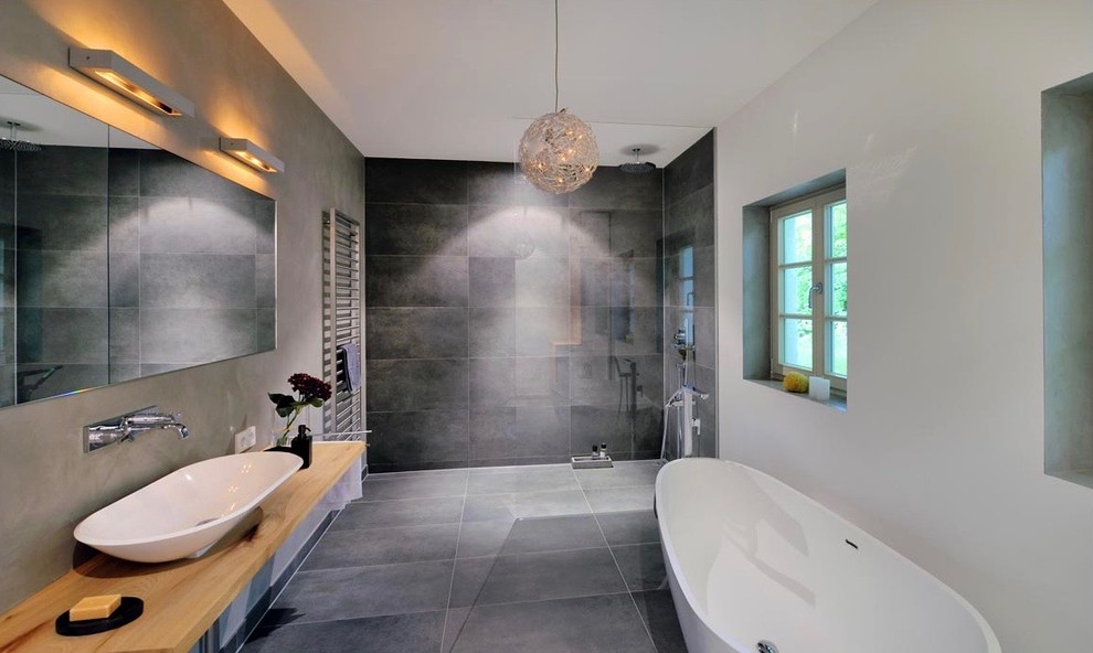 Foto på ett stort funkis badrum med dusch, med öppna hyllor, bruna skåp, ett fristående badkar, en kantlös dusch, en vägghängd toalettstol, stenkakel, vita väggar, cementgolv, ett fristående handfat, marmorbänkskiva, grått golv och med dusch som är öppen