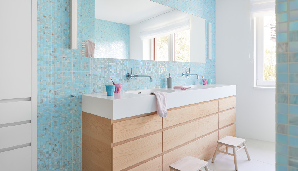 На фото: детская ванная комната в современном стиле с плоскими фасадами, светлыми деревянными фасадами, синей плиткой, разноцветной плиткой, плиткой мозаикой, белыми стенами, монолитной раковиной, белым полом, белой столешницей, тумбой под две раковины и напольной тумбой