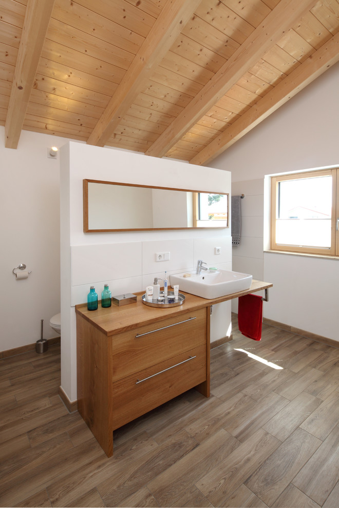 This is an example of a medium sized rural shower room bathroom in Munich with white tiles, a vessel sink, wooden worktops, an open shower, flat-panel cabinets, medium wood cabinets, a wall mounted toilet, ceramic tiles, white walls, medium hardwood flooring, brown floors and brown worktops.