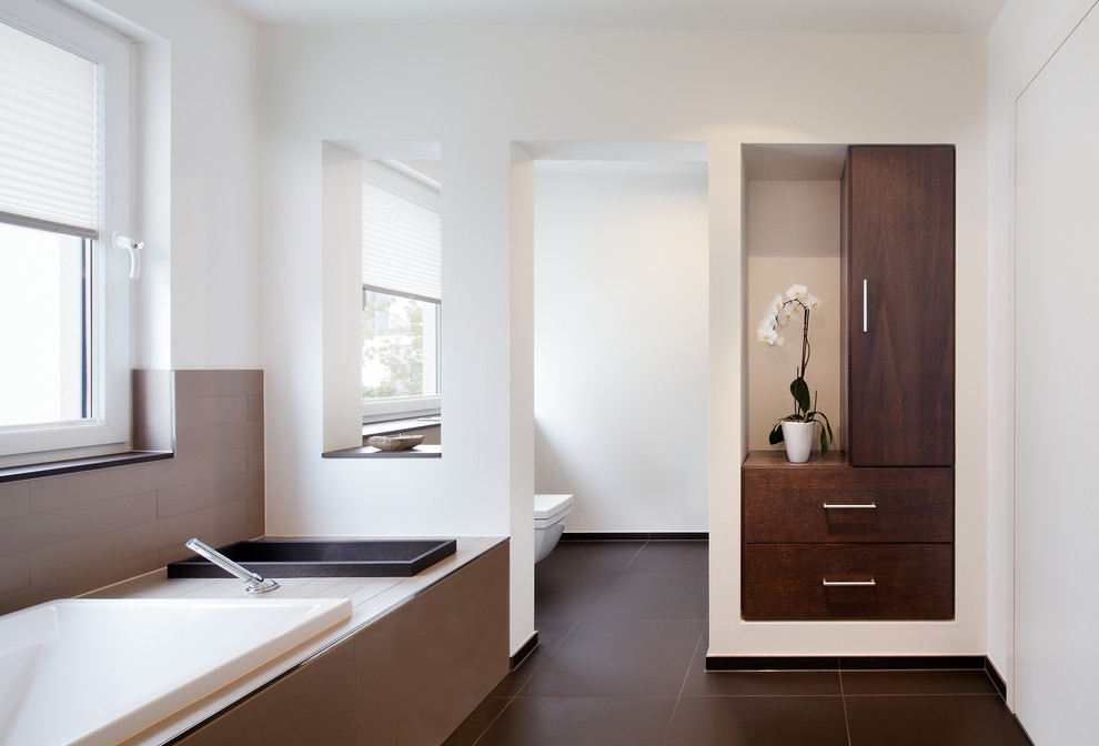 Idée de décoration pour une grande salle de bain design en bois foncé avec un placard à porte plane, une baignoire posée, un mur blanc et un carrelage gris.