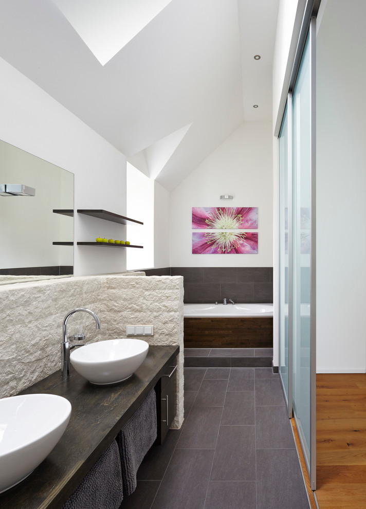 Großes Modernes Badezimmer mit Aufsatzwaschbecken, Einbaubadewanne, grauen Fliesen, Steinplatten, weißer Wandfarbe, Schieferboden und Waschtisch aus Holz in Köln