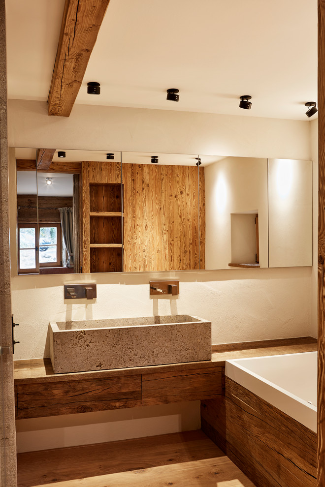 Photo of a small rustic shower room bathroom in Munich with flat-panel cabinets, medium wood cabinets, a built-in bath, a shower/bath combination, white walls, painted wood flooring, a vessel sink, wooden worktops and brown floors.