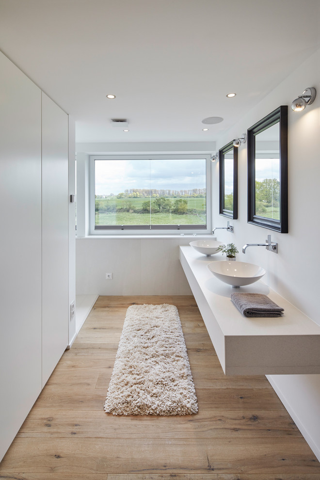 Exemple d'une salle de bain principale et longue et étroite tendance de taille moyenne avec un mur blanc, une vasque, un plan de toilette en surface solide et parquet clair.
