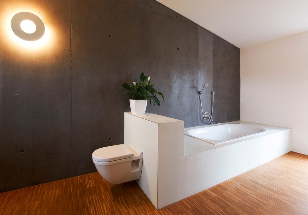 Example of a large trendy medium tone wood floor drop-in bathtub design in Stuttgart with a wall-mount toilet and black walls