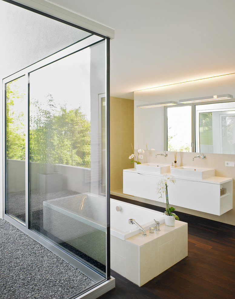 Стильный дизайн: большая ванная комната в современном стиле с настольной раковиной, плоскими фасадами, белыми фасадами, белыми стенами, темным паркетным полом, отдельно стоящей ванной и бежевой плиткой - последний тренд