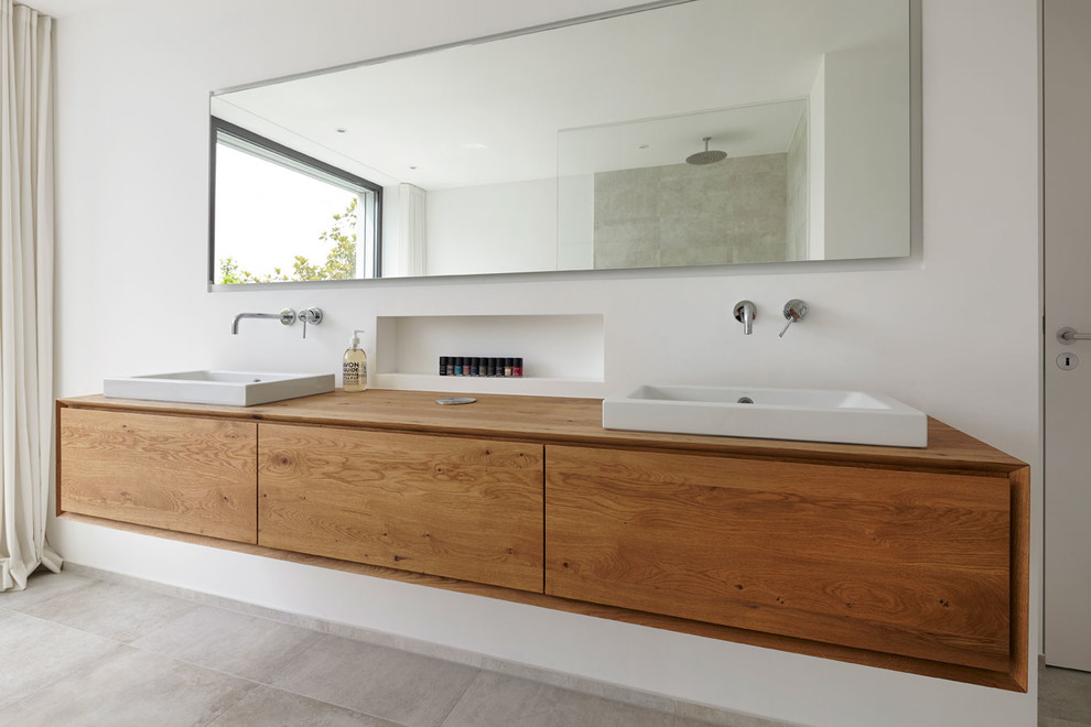 Modern inredning av ett brun brunt badrum med dusch, med släta luckor, skåp i ljust trä, ett fristående badkar, en kantlös dusch, beige kakel, kakelplattor, beige väggar, ett fristående handfat, träbänkskiva och med dusch som är öppen