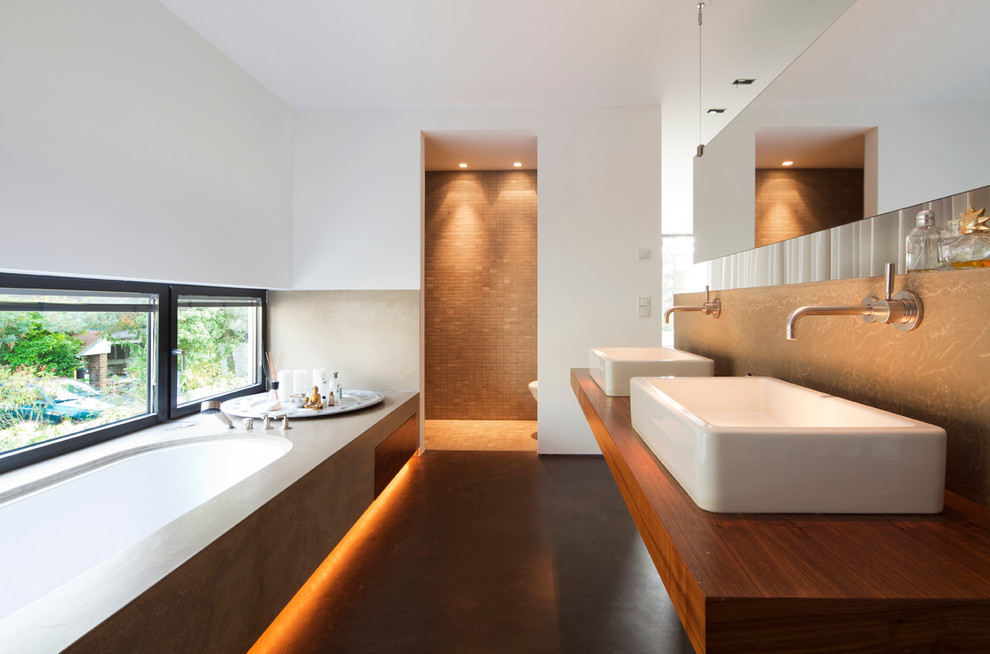 Cette image montre une grande salle de bain longue et étroite minimaliste avec un plan de toilette en bois, une baignoire encastrée et un plan de toilette marron.