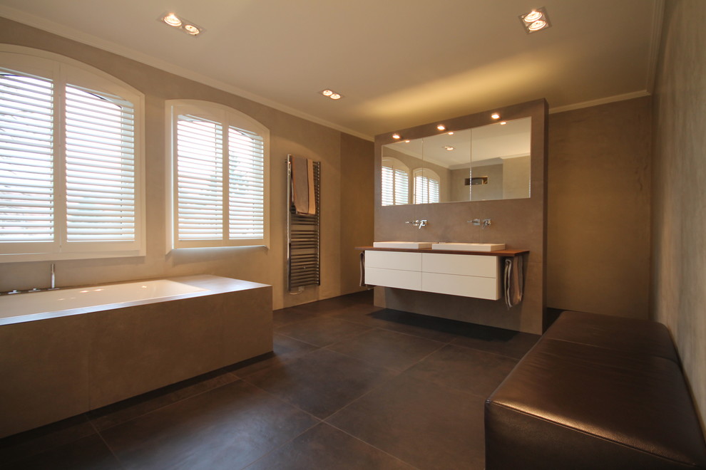 Imagen de cuarto de baño tradicional con puertas de armario blancas, bañera encastrada, baldosas y/o azulejos grises, paredes grises, aseo y ducha y lavabo sobreencimera
