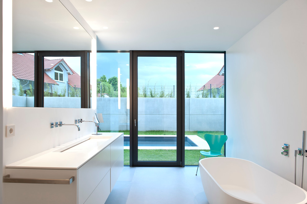 Mittelgroßes Modernes Badezimmer mit flächenbündigen Schrankfronten, weißen Schränken, freistehender Badewanne, weißer Wandfarbe, Betonboden und integriertem Waschbecken in Sonstige